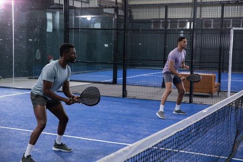 Male doubles players practicing padel on indoor blue court with paddles and net, training