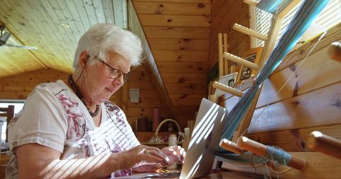 Senior Woman Working on Laptop in Artisan Workshop with Loom