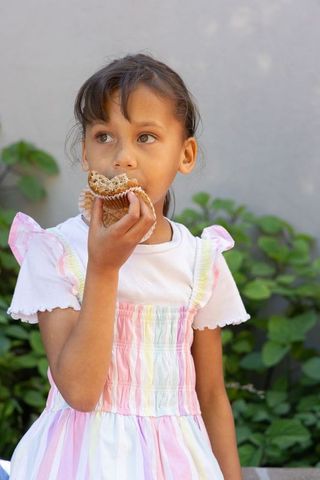 Young girl eating muffin in pastel striped dress outdoors in garden