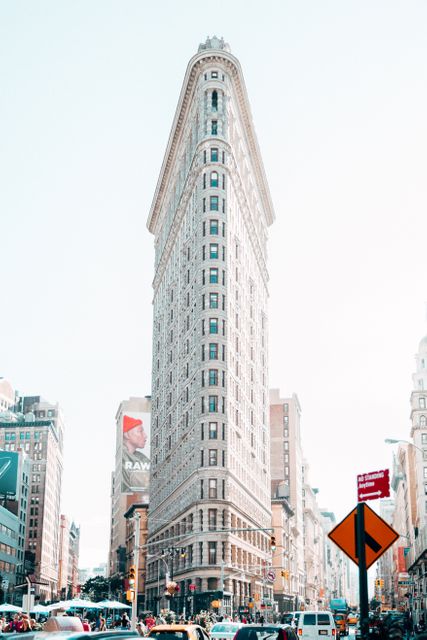 The image shows the Flatiron Building, an iconic landmark in New York City, surrounded by bustling streets filled with traffic and people. The photo captures the energetic atmosphere of Manhattan and is ideal for use in travel articles, city guides, architecture features, and marketing materials showcasing New York City's urban life and landmarks.