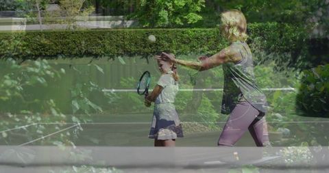 Mother Coaching Daughter in Tennis on Sunny Garden Court