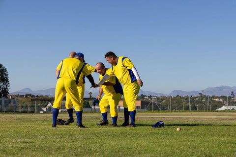 Veteran baseball teammates huddling in yellow and blue uniforms on outfield grass