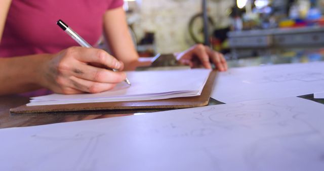 Young Caucasian woman sketches on paper at a workshop, with copy space. Her focus on the creative process highlights artistic dedication in a home studio setting.