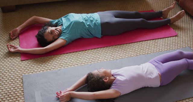 Mother and daughter lying on yoga mats, stretching arms above heads. Great for depicting family bonding, at-home fitness routines, parent-child activities, and promoting healthy lifestyles.