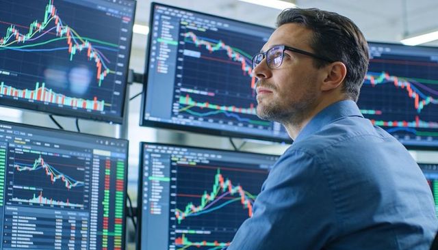 Trader analyzing multiple market charts on multi-monitor trading desk for active investing