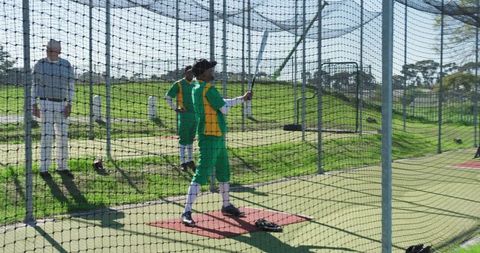Youth cricket practicing batting drills in outdoor net with coach supervising under sunlight