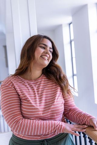 Smiling african american woman leaning on handrail in bright modern corridor, daylight