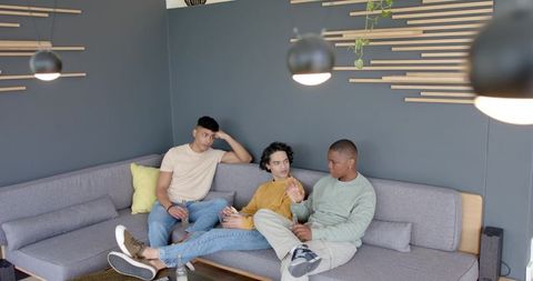 Diverse young men lounging on modern sofa sharing smartphone and casual conversation