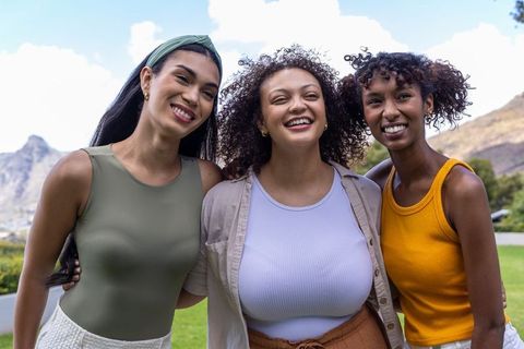Smiling diverse female friends embracing on sunny hillside during summer outing
