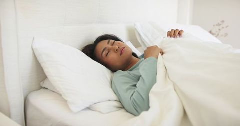 Mid-adult asian woman sleeping peacefully in minimalist neutral bedroom with soft linens