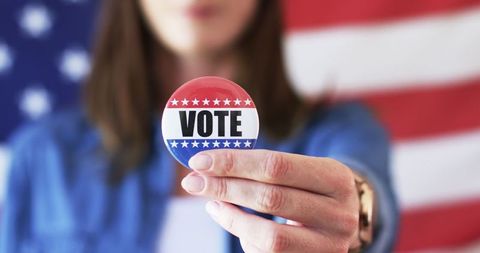 Woman holding vote button with american flag background