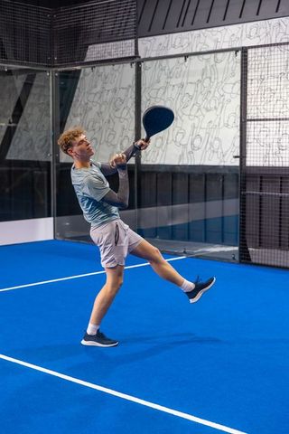 Young athlete executing overhead smash on modern indoor padel court with vibrant blue turf