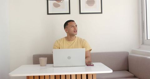 Young man working at home office nook with laptop and coffee in natural light, minimal decor