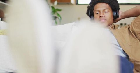 Relaxing young man listening to music on sofa with blurred feet foreground