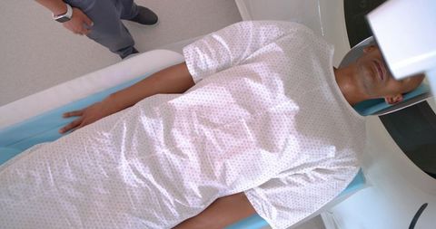 African american technician preparing male patient for mri scan lying supine in hospital