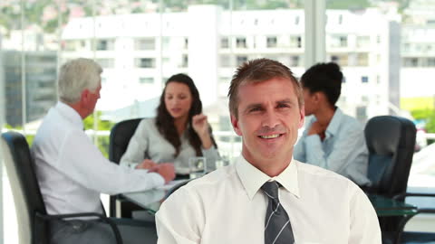 Confident Businessman with Team Meeting in Background in Bright Office