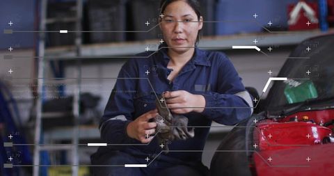 Female mechanic inspecting and cleaning engine part in workshop with red car and rag