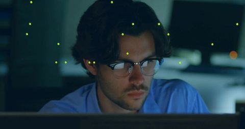 Young developer focusing on code on late-night monitors with glasses reflection and tracking markers