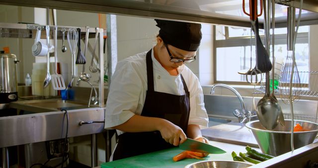 Female chef slicing vegetables in a professional kitchen indicating expertise in culinary arts. Ideal for use in promoting cooking classes, restaurant advertisements, culinary school brochures, and food blogging.