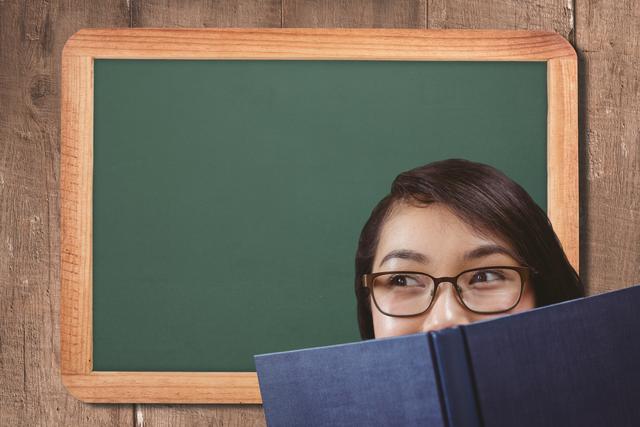 Digital composite of Close-up of woman with book against blackboard