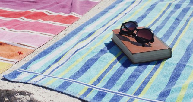 Image of sunglasses, book, towels and beach equipment lying on beach. Holidays, vacations, relax and beach concept.