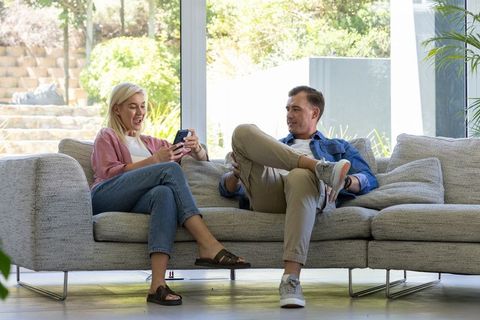 Couple relaxing on modern sofa sharing smartphone moment in bright minimalist living room