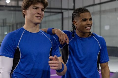 Two teammates smiling and pointing on indoor court wearing matching blue athletic shirts
