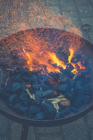 Sparks flying from charcoal grill as orange flames dance over wood and hot coals