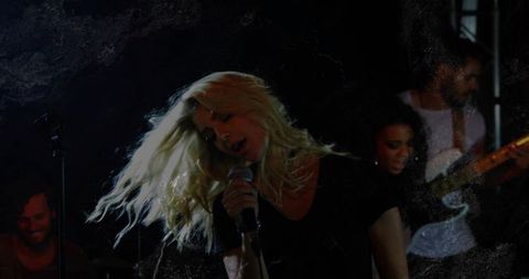 Blond Lead Singer Rocking Microphone on Moody Low-Light Stage with Live Band Energy and Backing Musi