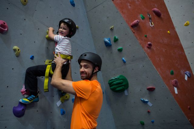 Trainer assists young child in rock climbing at indoor fitness studio. Great for articles on children sports, safety in climbing, fitness coaching, and indoor adventure activities.
