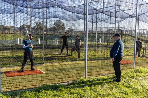 Coach signaling outside batting cage while batter swinging bat during baseball practice