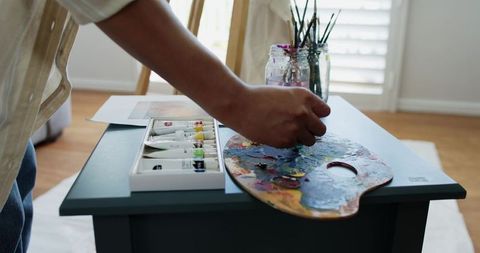 African American artist mixing vibrant paint on wooden palette in sunlit art studio