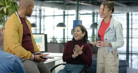 Diverse team celebrating success in modern open-plan office with charts and coffee