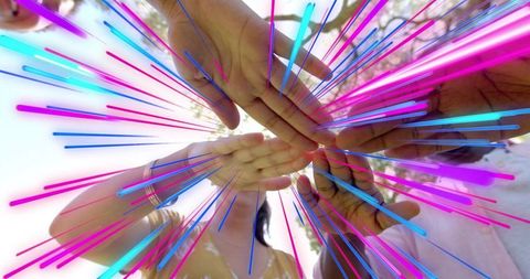 Uniting hands overhead with neon light streaks celebrating teamwork and collaboration
