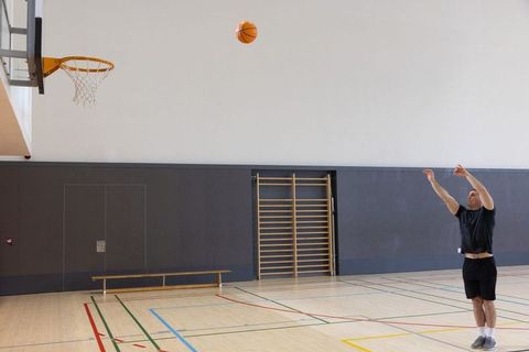 Male athlete shooting jump shot on indoor gym court toward left hoop during practice