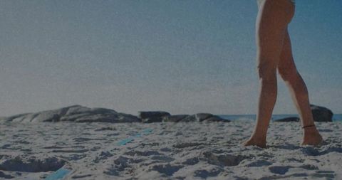 Woman standing barefoot on sandy beach wearing anklet and bikini bottom coastal sunlight