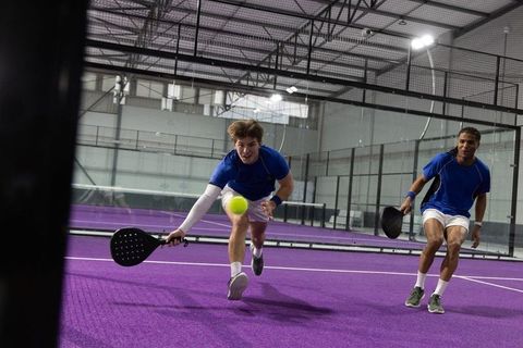 Indoor padel doubles lunging to reach ball on vibrant purple court with black paddles