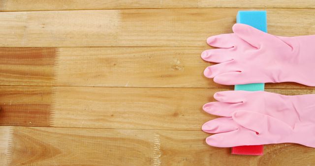 Hands in pink gloves are scrubbing a wooden surface with a blue sponge, with copy space. Cleaning and maintenance of wooden surfaces are essential for their longevity and aesthetic appeal.