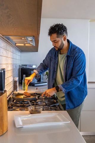 Man cooking burger on gas stove wearing smartwatch and denim jacket in modern kitchen