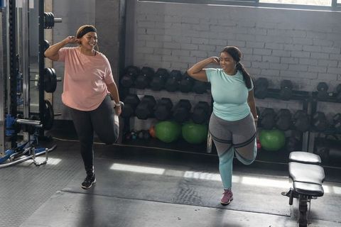 African american women stretching and balancing during gym workout near dumbbells