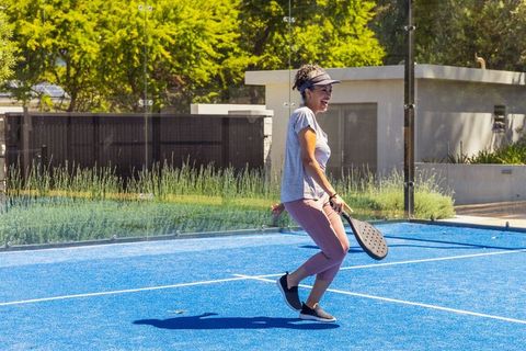 Joyful african american woman playing padel on bright blue court in sunny outdoor recreation