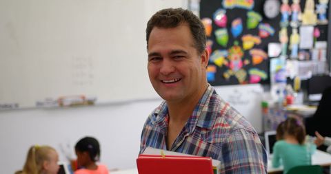 Smiling Male Teacher Holding Books in Vibrant Classroom - Download Free Stock Images Pikwizard.com