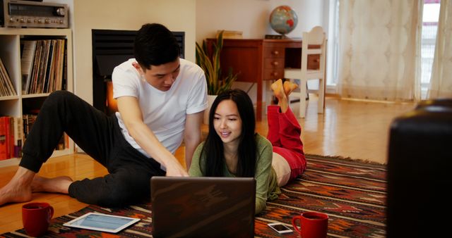 Young couple spending time together in a cozy living room, using a laptop for browsing or streaming. Ideal for themes of modern lifestyle, technology in daily life, teamwork, and home leisure activities.