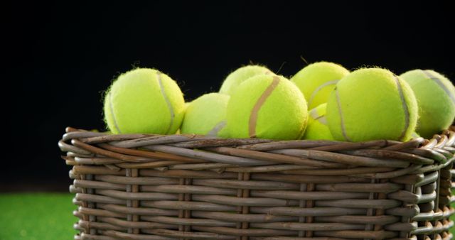 Perfect for sports-related content, this image features a wicker basket filled with yellow tennis balls placed on a grass court. Suitable for promoting tennis equipment, sports events, recreation activities, or fitness routines.