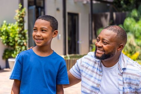 African american father kneeling with son smiling outside home showing togetherness