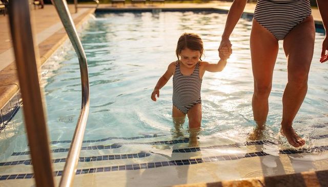 Mother and daughter walking on pool steps in matching striped swimsuits during golden hour