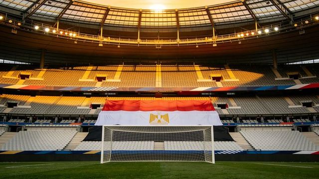 Sunlit empty stadium with egyptian flag draped over stands behind football goal