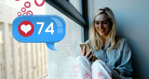 Smiling Woman Checking Social Media on Phone by Window