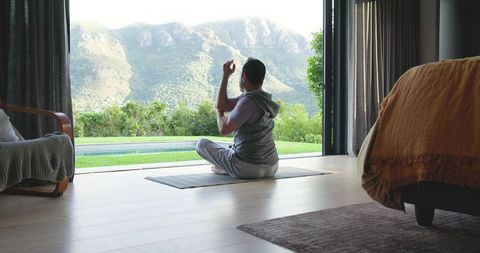 Man Meditating Indoors Near Open Glass Doors with Scenic Mountain View