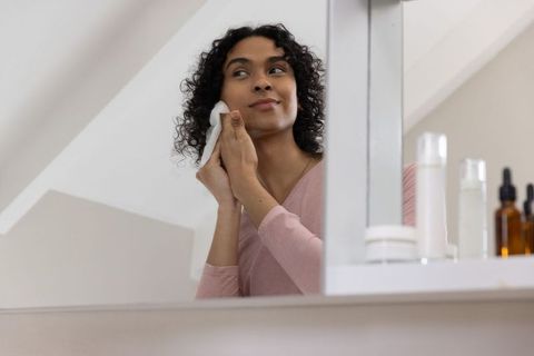 Nonbinary person doing skincare at mirror under sloped ceiling, minimal calming routine